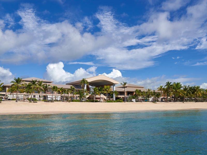 Strand met zand, palmbomen en een resort onder een blauwe lucht