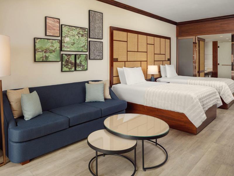 Moderne hotelkamer met twee bedden, bank, tafels en wanddecoratie.