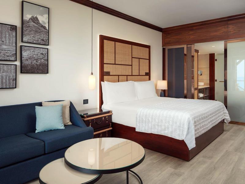 Modern hotelkamer met tweepersoonsbed, blauwe bank en ronde salontafel