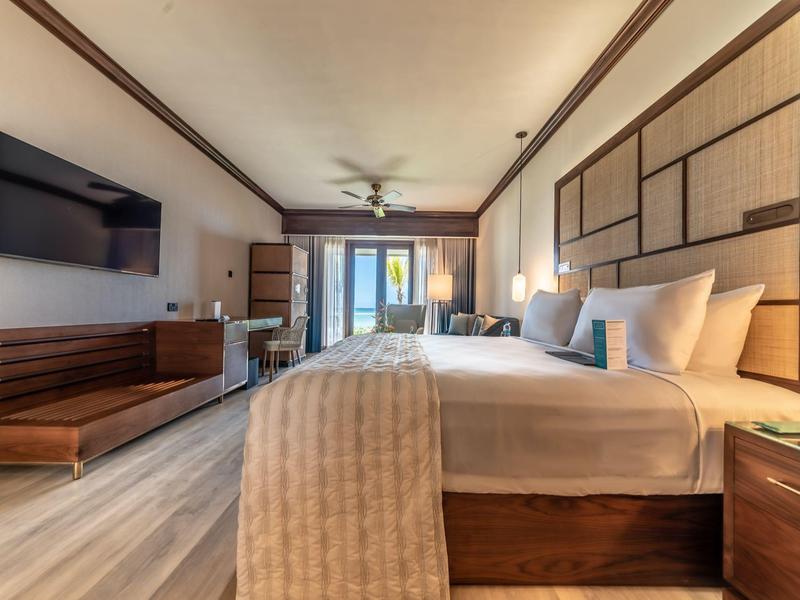 Modern hotelkamer met tweepersoonsbed, tv, plafondventilator en balkon met zeezicht.