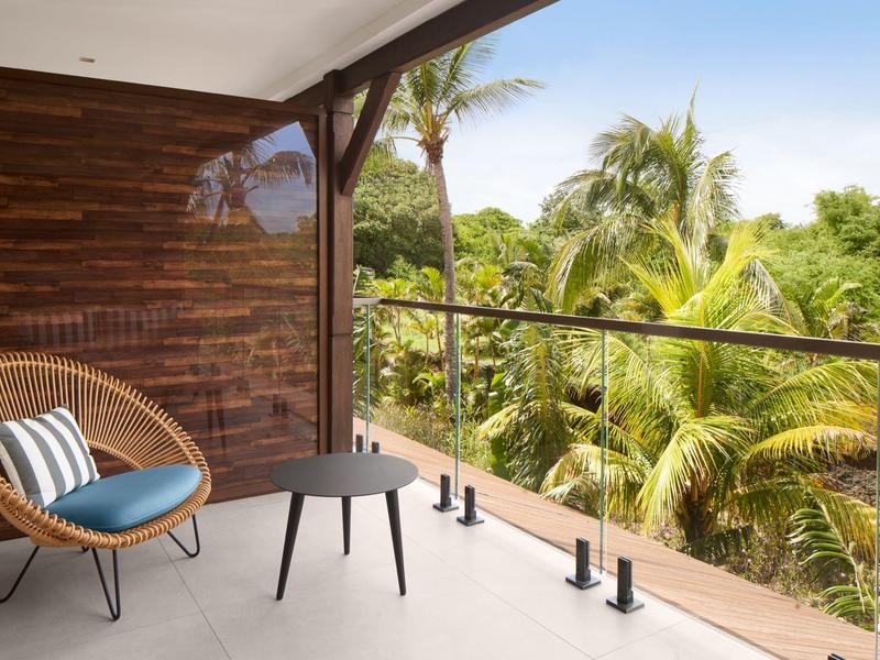 Balkon met rotan stoel, blauw kussen, tafel en uitzicht op tropische palmbomen