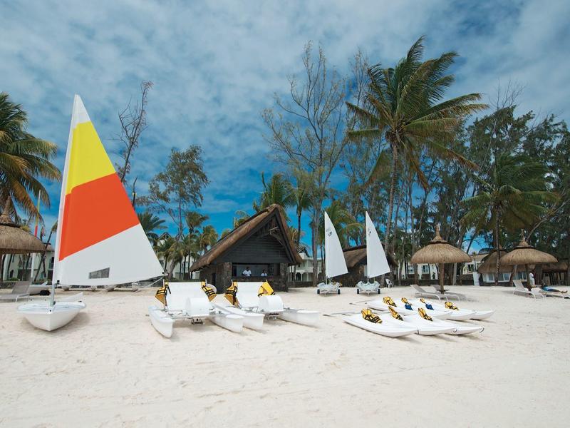 Segelboote mit bunten Segeln stehen am weißen Sandstrand unter Palmen bei blauem Himmel.