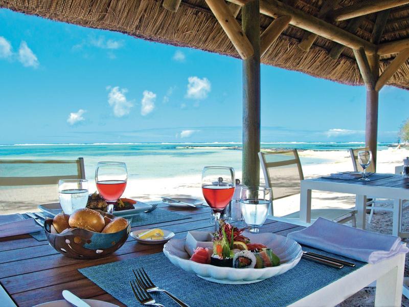 Strandrestaurant mit gedecktem Holztisch, Meerblick, blauem Himmel und frischem Essen.