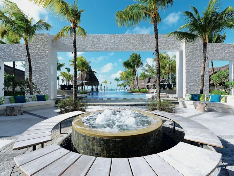 Moderner Außenbereich mit Whirlpool, Palmen und Blick auf türkisfarbenes Meer unter blauem Himmel.