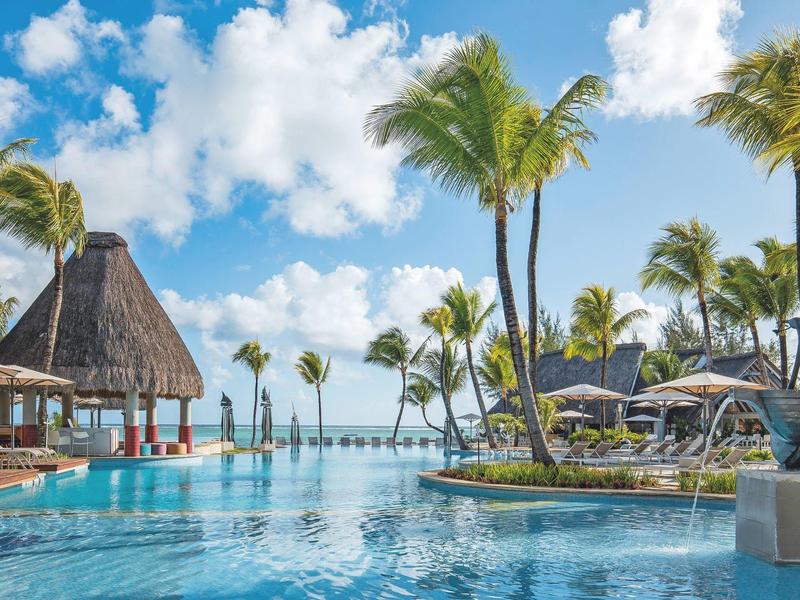 Großer Pool mit Palmen, Liegestühlen und blauem Himmel in tropischer Resort-Umgebung.