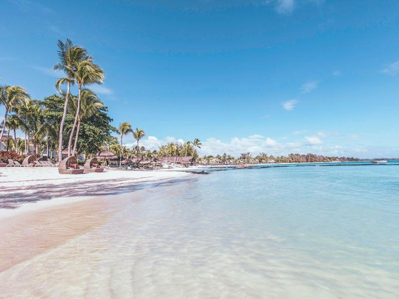 Klarer flacher Strand mit weißen Sand und Palmen unter blauem Himmel am tropischen Meer.