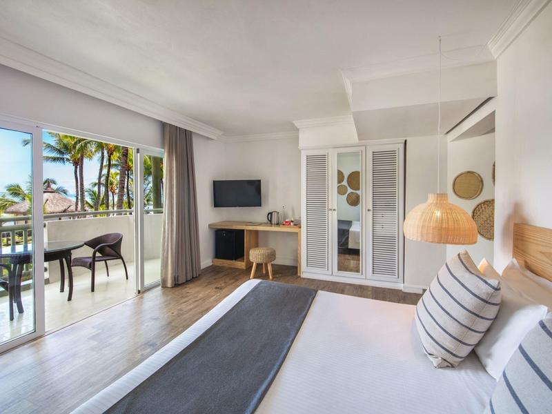 Helles Schlafzimmer mit Doppelbett, TV, Schreibtisch, Balkon und Blick auf Palmen und blauen Himmel.