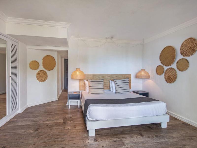 Schlichtes Schlafzimmer mit Holzfußboden, Doppelbett, Nachttischen und dekorativen Körben an den Wänden.