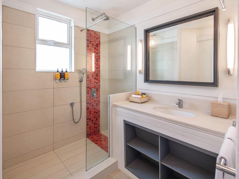 Helles Badezimmer mit großer Walk-in-Dusche, Waschbecken, Spiegel und offenem Regal unter der Arbeitsplatte.