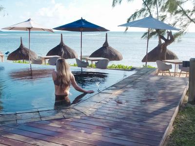Frau im Pool mit Strohdach-Sonnenschirmen und Blick auf das blaue Meer bei sonnigem Wetter.