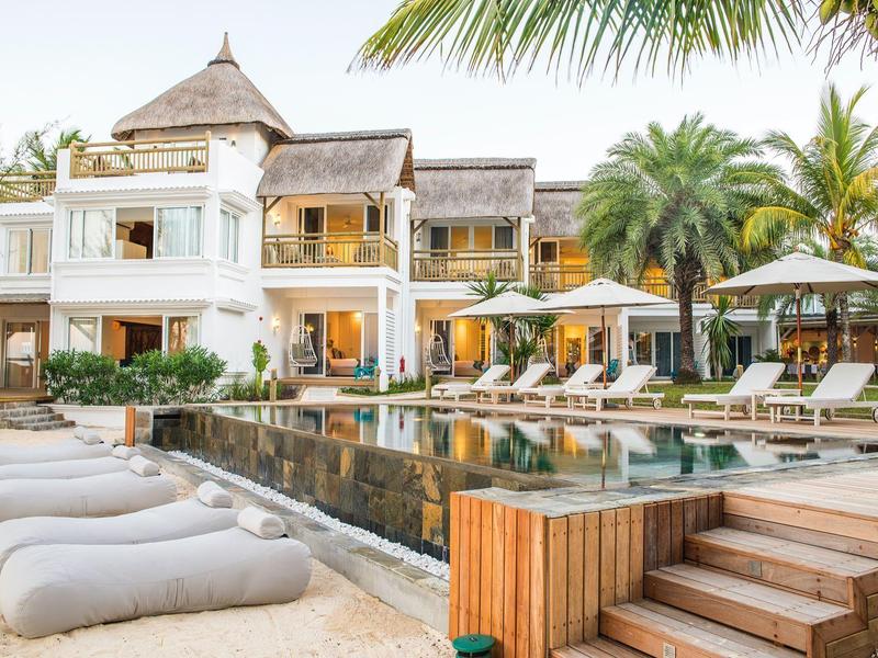 Luxe hotel met zwembad, ligstoelen en palmbomen in tropische omgeving.