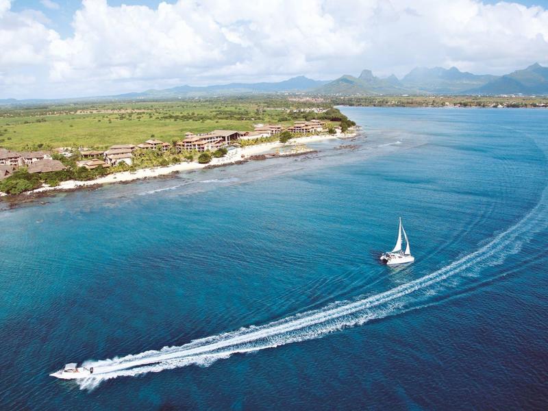 Sailboat and motorboat on blue water near a coastline with green landscape and mountains in the background.