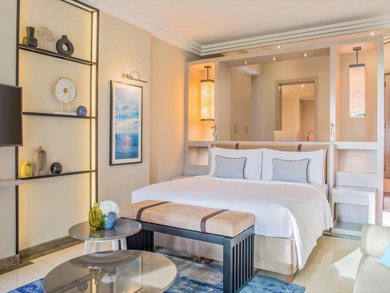 Modern hotel room with large bed, nightstands, and cozy seating area.