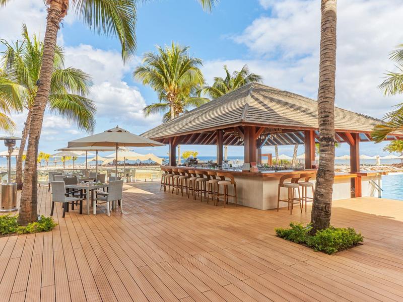 Open bar with wooden deck and palm trees at a beach resort during daylight.