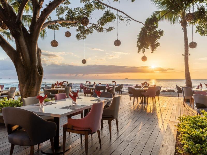 Seaside restaurant terrace with sunset and set outdoor tables.