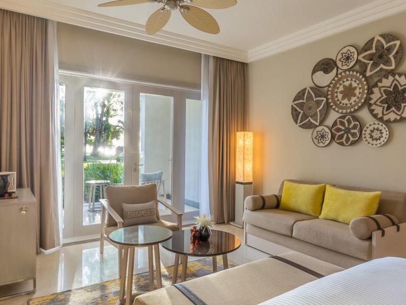 Cozy hotel room with comfortable seating area, decoration, and balcony access with garden view.