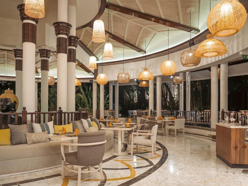 Modern open hotel restaurant with round tables, chairs, and warm hanging lights.