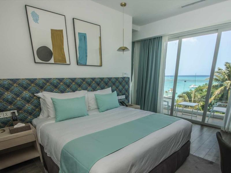 Modern hotelkamer met tweepersoonsbed en zeezicht door glazen ramen.