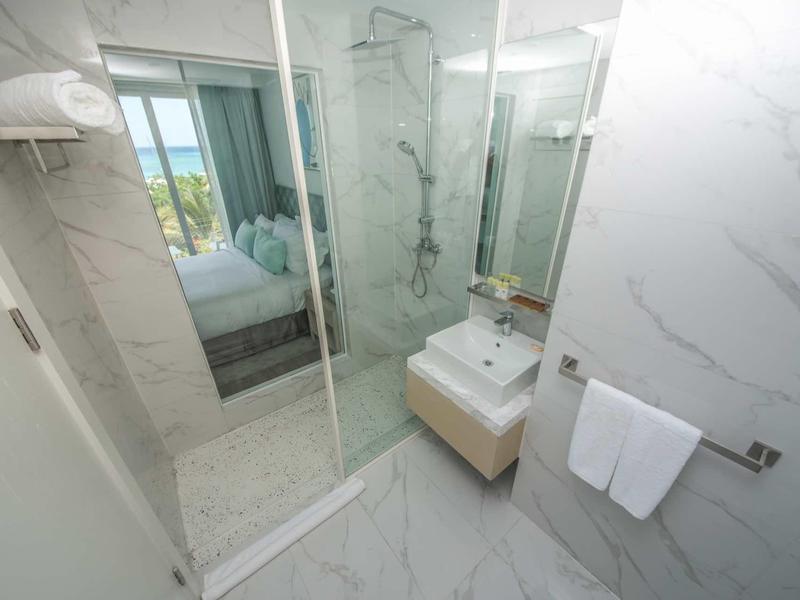 Moderne badkamer met glazen douche, wastafel, spiegel en uitzicht op slaapkamer en zee.