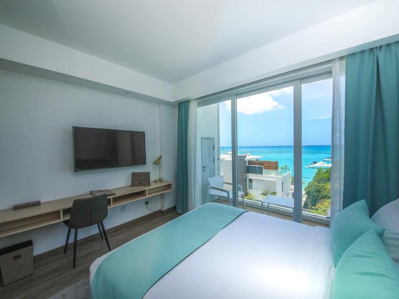 Moderne hotelkamer met groot bed, tv, bureau en zeezicht door grote glazen ramen.