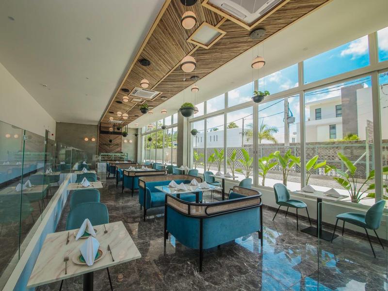 Modern restaurant met blauwe stoelen, grote ramen en houten plafond bij daglicht.