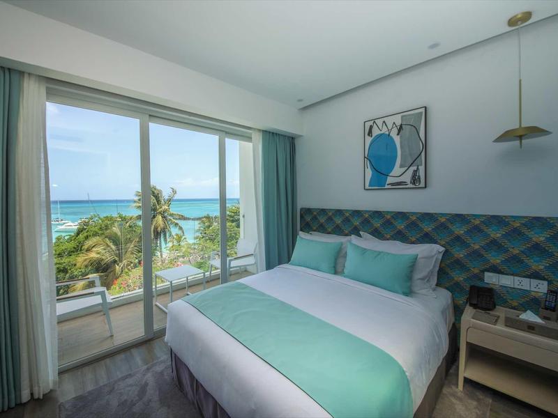 Hotelkamer met tweepersoonsbed, balkon toegang en zeezicht bij daglicht.