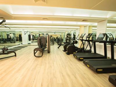 Moderner Fitnessraum mit Laufbändern, Crosstrainern und Kraftgeräten, heller Holzboden, Spiegelwand.
