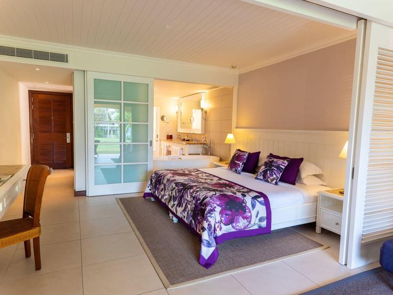 Moderne hotelkamer met tweepersoonsbed, bureau, comfortabele stoelen en badkamer op de achtergrond.