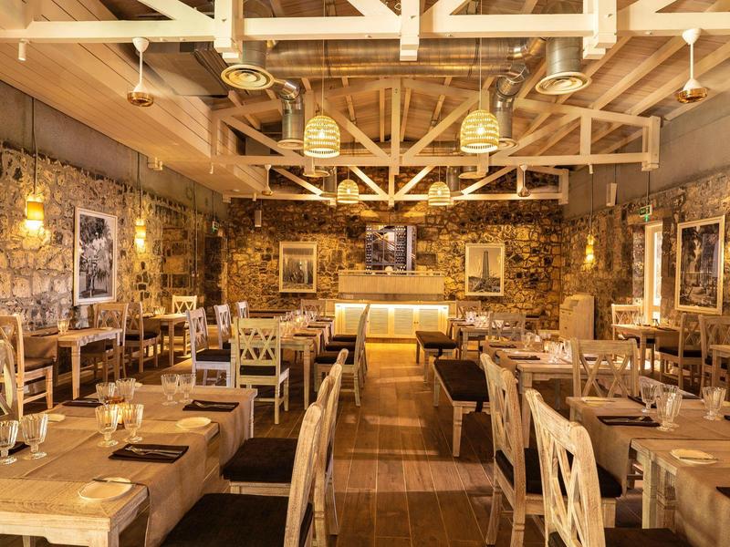 Rustiek restaurant met houten tafels, stoelen en warme verlichting in een kamer met stenen muren