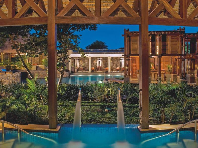 Uitzicht op een verlicht zwembad en omliggende gebouwen in een hotelcomplex bij schemering.