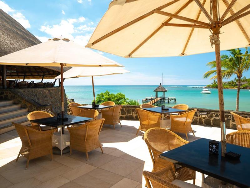 Zonnig buitenterras van een hotel met parasols en rotan stoelen met uitzicht op zee.