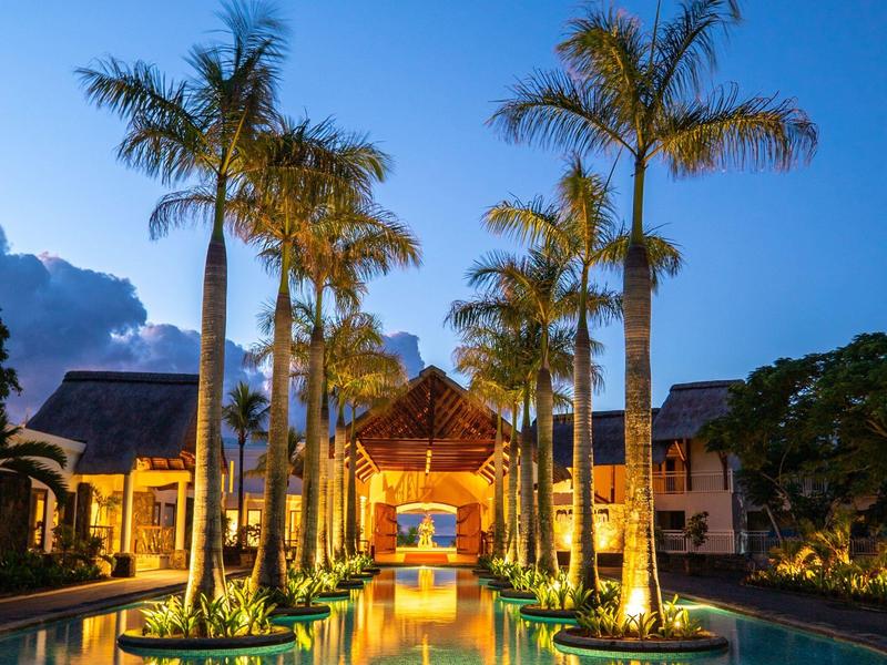 Verlichte zwembadomgeving met palmbomen en tropisch hotelgebouw bij zonsondergang