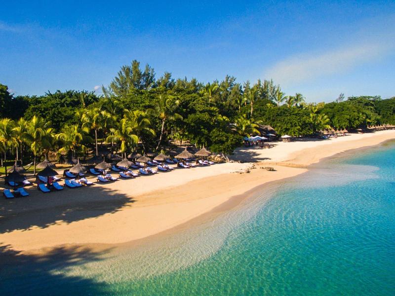 Strand met parasols en ligstoelen bij tropische begroeiing en helder water
