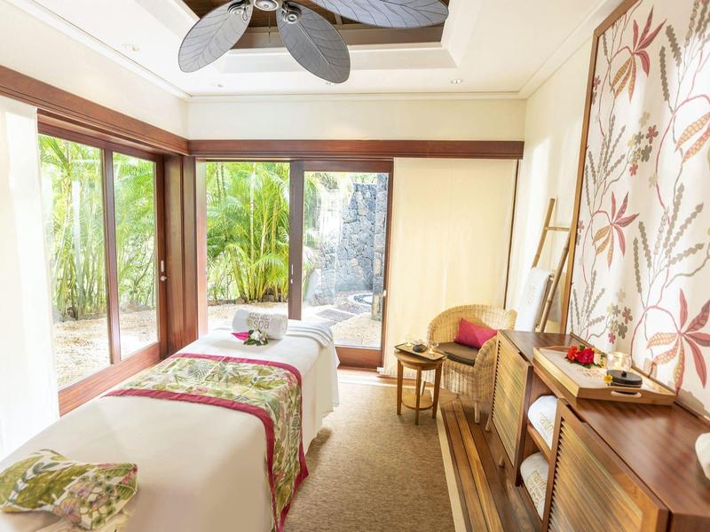 Lichte spakamer met twee massagetafels, decoratieve wandkunst en groot raam met uitzicht op groen.