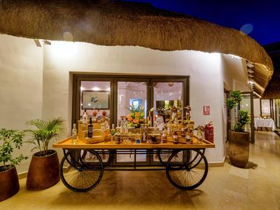 Beleuchteter Getränkewagen vor einem Gebäude mit strohgedecktem Dach in der Dämmerung.