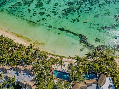 Strand mit türkisfarbenem Wasser, weißen Sand, Palmen und Gebäuden am Ufer aus der Vogelperspektive.