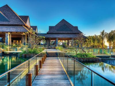 Luxe villa met houten loopbrug over waterbekkens en donkere dakpannen onder blauwe lucht