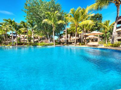Helles Schlafzimmer mit weißer Bettdecke, Holzmöbeln, Deckenventilator und Blick auf grüne Natur.