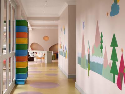 Gang met kleurrijke muurschilderingen en felgekleurde kussens naast glazen wanden in een hotel.