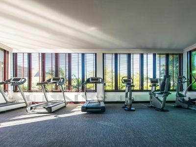 Heller Fitnessraum mit Laufbändern und Fitnessgeräten vor großen Fenstern