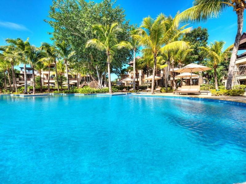 Groot zwembad met helder blauw water en palmbomen omgeven door hotelgebouwen onder een zonnige lucht.