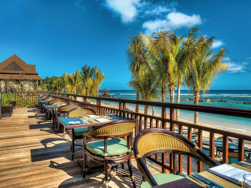 Terras met zithoek naast palmbomen en uitzicht op zee bij heldere blauwe lucht.