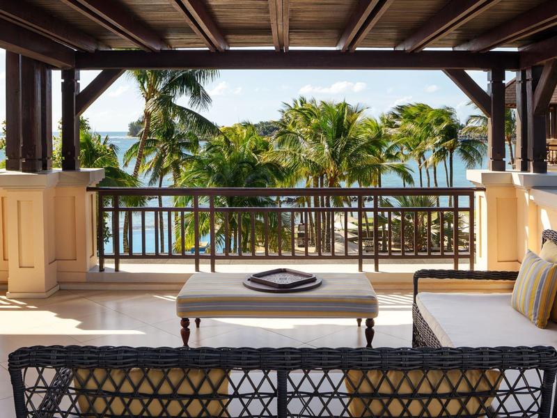 Uitzicht vanaf een overdekt terras met uitzicht op tropische palmbomen en de zee bij een hotel.