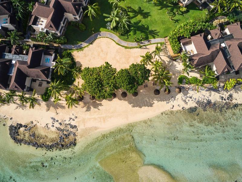 Luchtfoto van strandbungalows naast helder turquoise water en zandstrand.