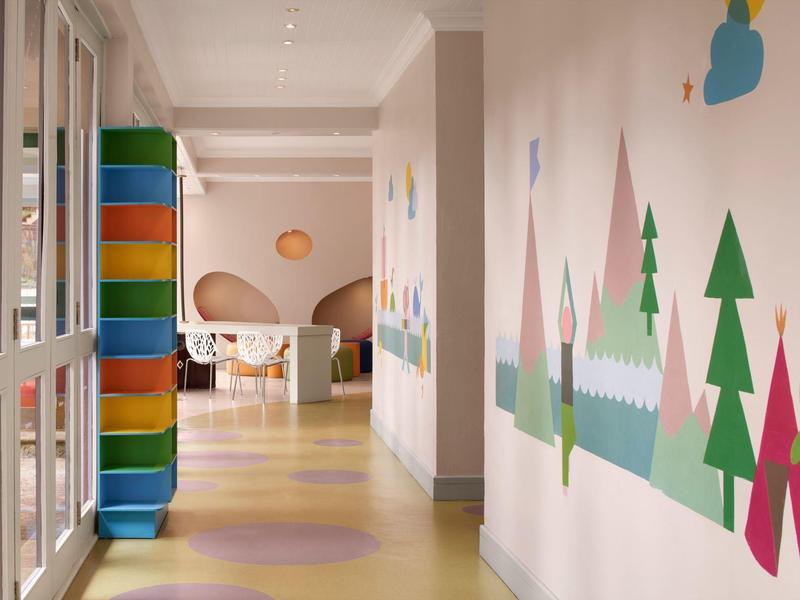 Gang met kleurrijke muurschilderingen en felgekleurde kussens naast glazen wanden in een hotel.