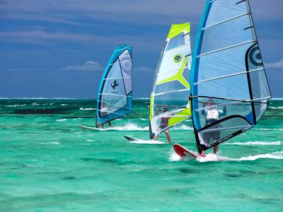 Drei Surfer segeln auf türkisblauem Wasser unter blauem Himmel.