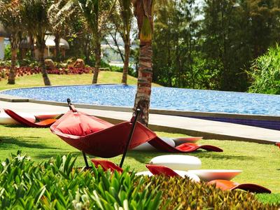 Leżaki i czerwone parasole obok basenu w zielonym ogrodzie.