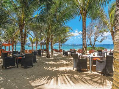 Strandrestaurant mit Tischen und Stühlen unter Palmen am Meer.