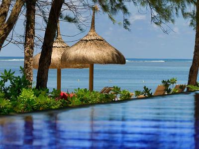 Blauer Pool mit Blick auf das Meer und Strohdachpavillons, umgeben von Bäumen und Pflanzen.