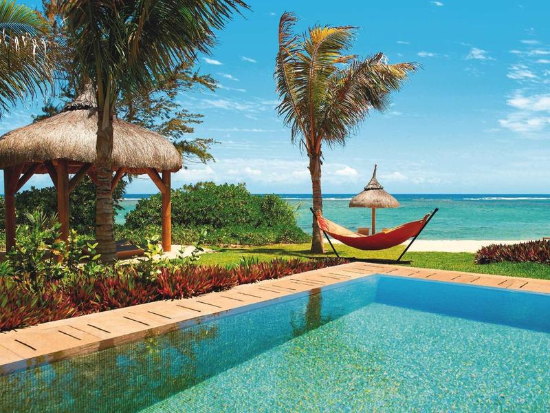 Basen z palmami, hamakiem i widokiem na niebieskie morze pod niebieskim niebem.